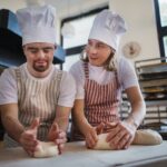 Man with down syndrom helping prepair bread in bakery with his colleague. Concept of integration